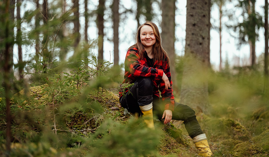 Anne-Mari Tarkkio istuu sammalmättäällä omassa metsässään. 